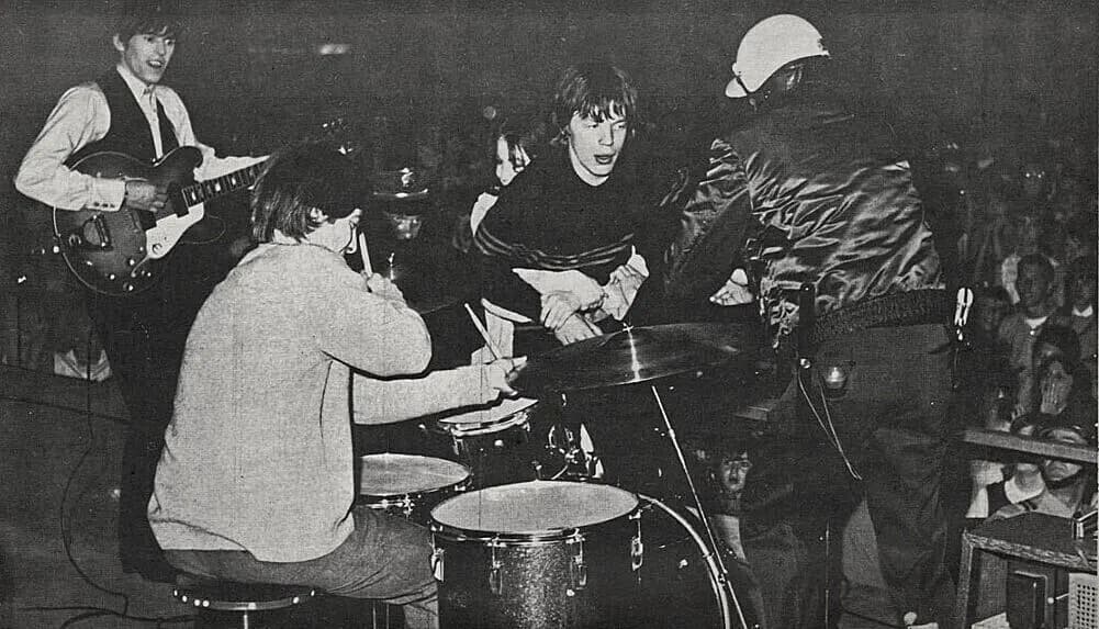 Jagger is rushed on stage by a female fan during a 1965 performance in West Germany. Image has been GRAYSCALED