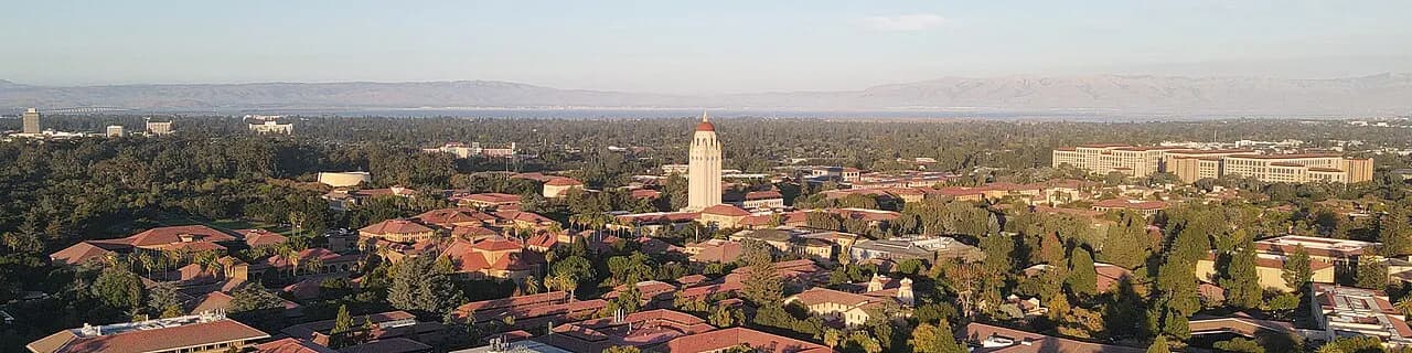 The image is an aerial view of Stanford University, featuring the campus buildings with distinctive red-tile roofs. At the center of the image is the iconic Hoo