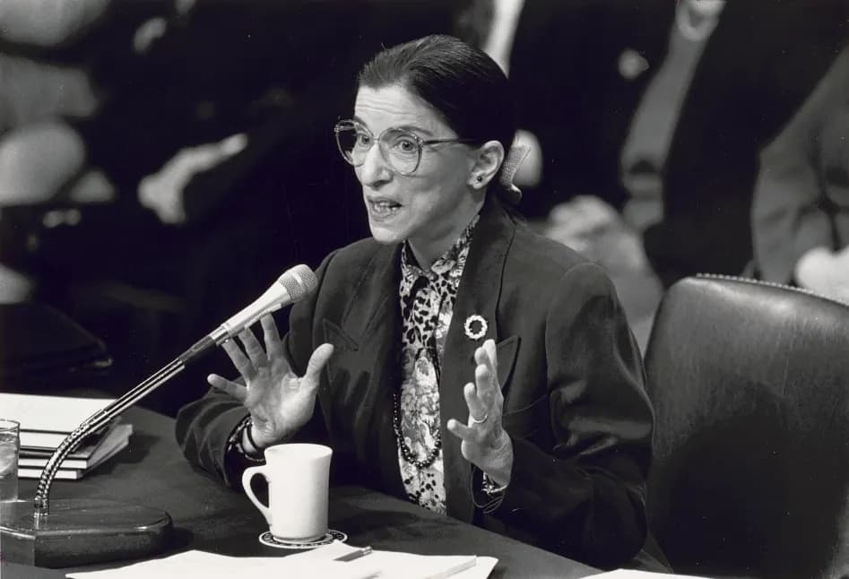 Photograph shows Ruth Bader Ginsburg speaking into microphone at Senate confirmation hearing for her appointment to the Supreme Court.